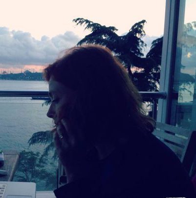 Wendy Wiseman turned in profile sitting at desk with ocean and sunset in background