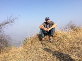 Ahmad Atif Ahmad sitting on a grassy hill with fog obscuring the distance